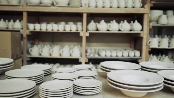 Білі керамічні чашки та тарілки знаходяться на полицях виробничого цеху — стокове відео