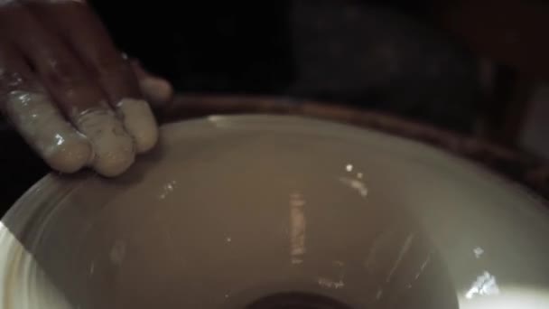 Close-up van een menselijke hand die een bord met witte verf op een pottenbakkerswiel schildert. — Stockvideo