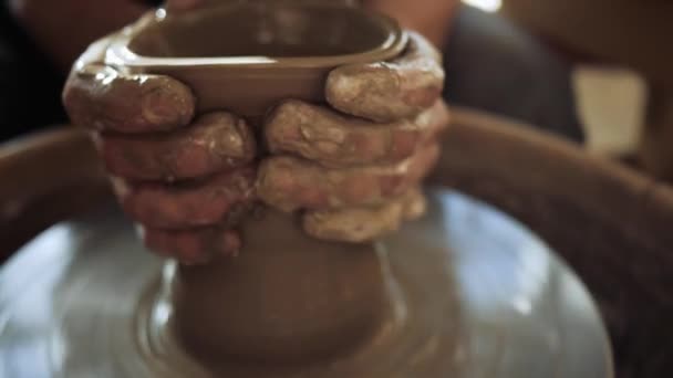 Een pottenbakker op een pottenbakkerswiel maakt een lange, smalle vaas van een brede kom. — Stockvideo