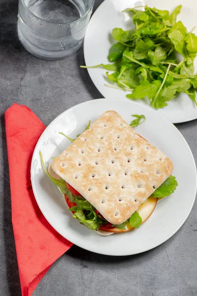 Dunne sandwich met kaas en salade op een wit bord — Stockfoto