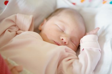 Newborn baby girl sleeping in her crib, lit by the morning sun