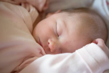 Newborn baby girl sleeping in her crib, lit by the morning sun