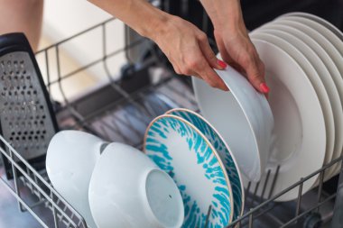 Kadın eli beyaz bir tabak bulaşık makinesi koyarak; bir househ