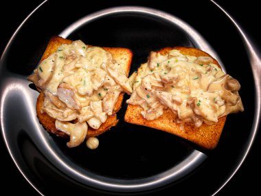 Krema soslu mantarlar ve kavrulmuş ekmekler. Mutfaktan siyah arka planda kalan detaylar.