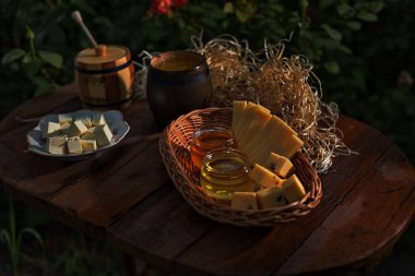 Lezzetli bal seti. Birçok kavanozdaki bal sıvıdır, raflardaki kilerde, yaratıcı bir fotoğraftır. Masada ekmek ve ekmek parçaları olan baldır. Ve gün batımında peynir, ışıkla, lezzetli yiyeceklerle, bahçede.