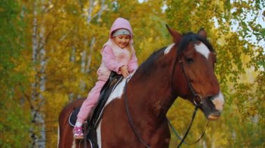 Küçük kız ata biniyor, sarılıyor ve okşuyor, çocuk ata biniyor.