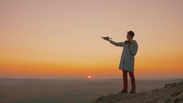 Homem em pé no topo da montanha, começa drone de sua mão, avião decola — Vídeo de Stock
