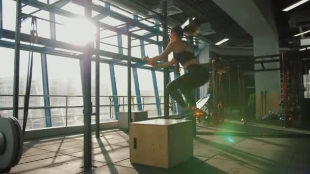 Mujer joven saltando en la caja de madera en el entrenamiento crossfit en el gimnasio — Vídeo de stock
