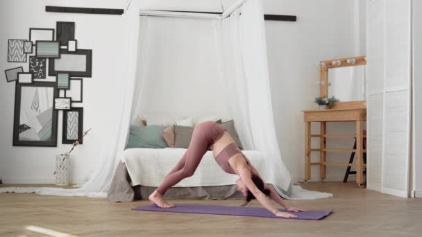 Mujer caucásica en ropa deportiva realiza yoga asanas pierna columpio en la habitación — Vídeo de stock