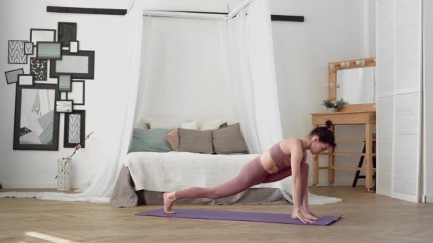 Mujer caucásica en ropa deportiva realiza yoga asanas pierna columpio en la habitación — Vídeos de Stock