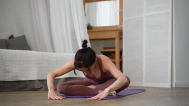 İnce, esnek, beyaz, orta yaşlı, siyah saçlı, bej eşofmanlı kadın. Asana namaste 'de duruyor. Mor yoga minderinde duruyor.