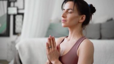 İnce, esnek, beyaz, orta yaşlı, siyah saçlı, bej eşofmanlı kadın mor yoga minderinin üzerinde asanas pranayamasını gevşetiyor.