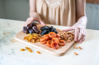 Masanın üzerindeki kurutulmuş kayısılar, kuru erikler, kuru üzümler, hurmalar ve bademler.
