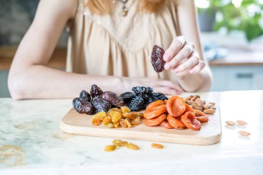Masanın üzerindeki kurutulmuş kayısılar, kuru erikler, kuru üzümler, hurmalar ve bademler.