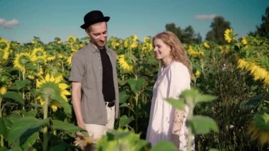 Şapkalı adam ayçiçeği tarlasında, bir buket kır çiçeği verir Genç sarışın