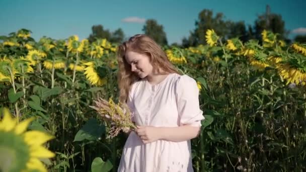 Chica con el pelo rizado en el campo de girasol con ramo de flores silvestres sonrisas — Vídeo de stock