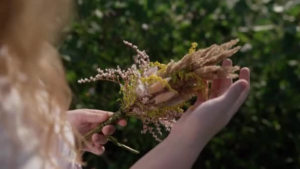 Chica con el pelo rizado en el campo de girasol con ramo de flores silvestres sonrisas — Vídeo de stock