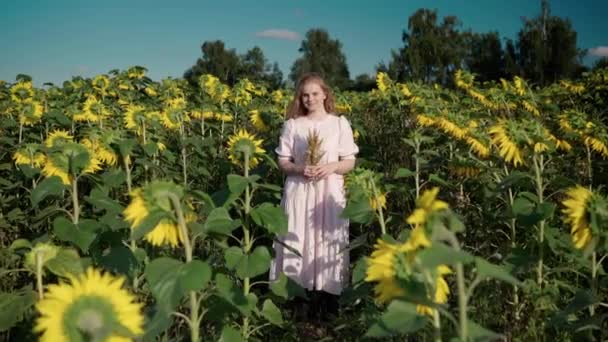Dziewczyna z kręconymi włosami na polu słonecznika z bukietem dzikich kwiatów uśmiecha — Wideo stockowe