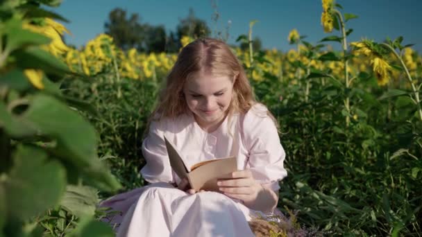 Uma jovem loira em um campo de girassol lê um livro, olha em volta, espera — Vídeo de Stock