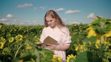 Ayçiçeği tarlasında genç sarışın bir kız kitap okuyor.