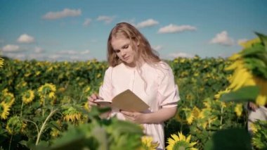 Ayçiçeği tarlasındaki genç sarışın kadın kitap okuyor, şapkalı adam kızların gözlerini kapatıyor.