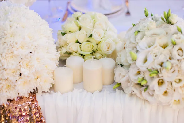 Wedding decor. Bouquet of white flowers and vwhite candles on gold background in restaurant.