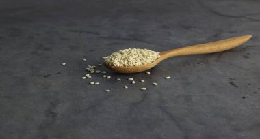 Siyah arkaplanın ortasında bir kaşık beyaz susam.