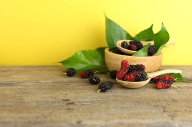 Close up of fresh mulberries and bowl of fruit against yellow background