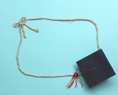 Education frame - Top view of rope frame tie as bow and graduated cap at the corner on light blue background