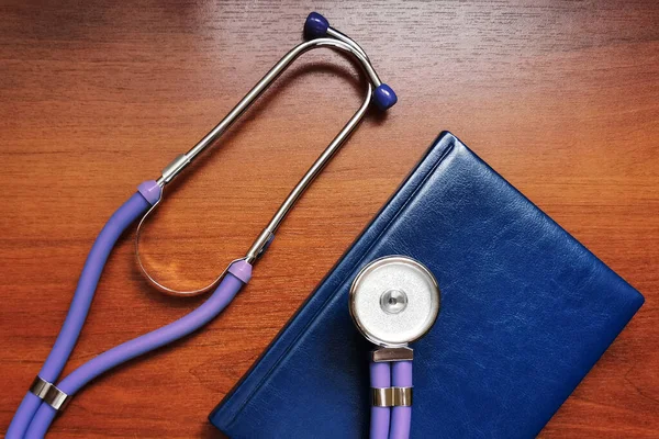 Purple stethoscope and notebook on a wooden background- medical tools