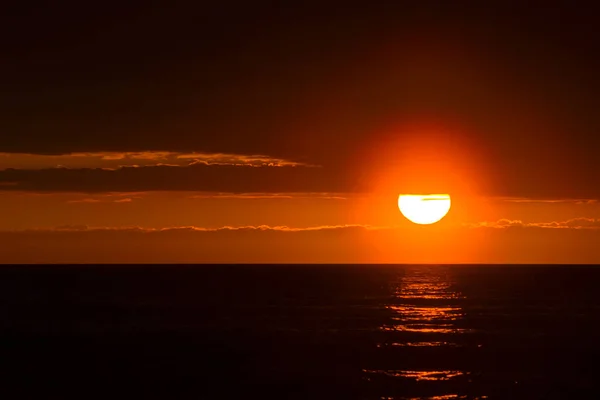 A large solar disk sits on the horizon in the background of the cloudy sky. Sunset on the baltic sea — Stock Photo, Image