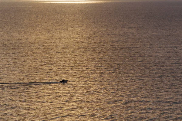 Marine golden surface with ripples at sunset. A small motor boat is sailing fast on the sea — Stock Photo, Image