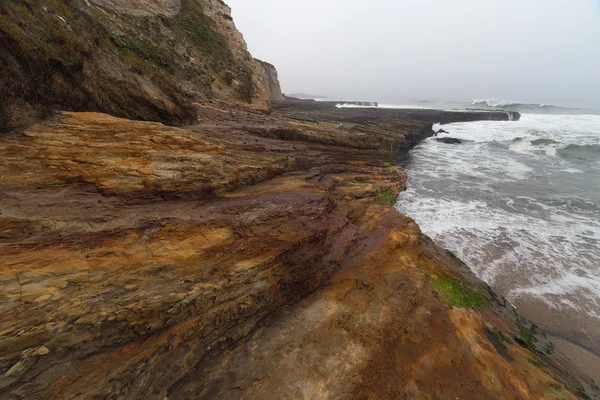 Ondas oceánicas que fluyen hacia abajo en rocas costeras rayadas —  Fotos de Stock