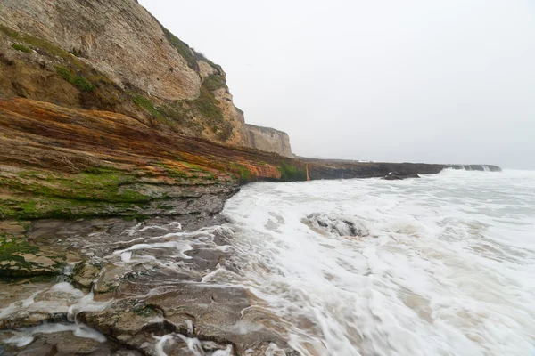 Ondas oceánicas que fluyen hacia abajo en rocas costeras rayadas —  Fotos de Stock