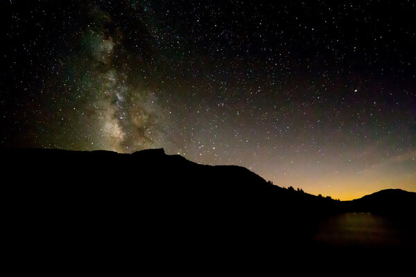 Milky Way above black silhouette of mountain with sunset glow re