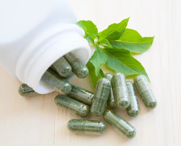 Herb capsules spilling out of a bottle — Stock Photo, Image