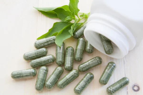 Herb capsules spilling out of a bottle — Stock Photo, Image