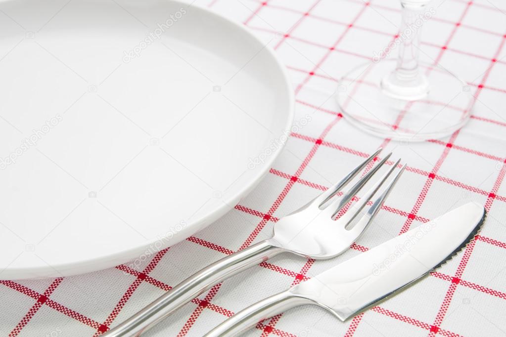 plate fork and knife on red napkin and wine glasses