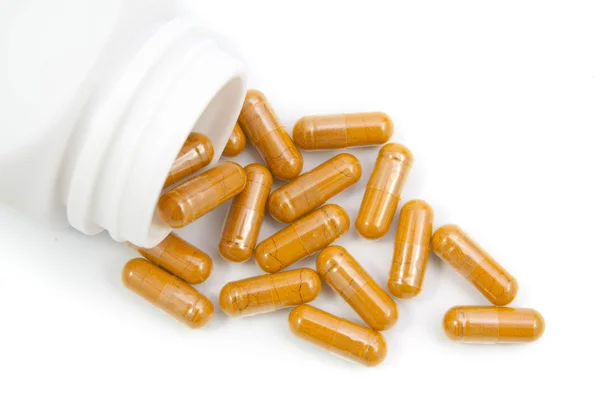 Herb turmeric capsules spilling out of a bottle  isolated on whi — Stock Photo, Image