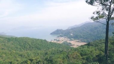 Deniz manzarası, tepeler ve arka planda yeşil ağaçlar.