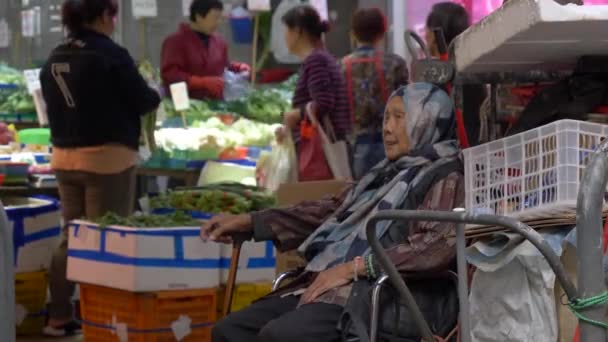 Hong Kong - 23 de enero de 2020: Vieja con pañuelo en la cabeza sentada en un mercado chino de alimentos — Vídeo de stock