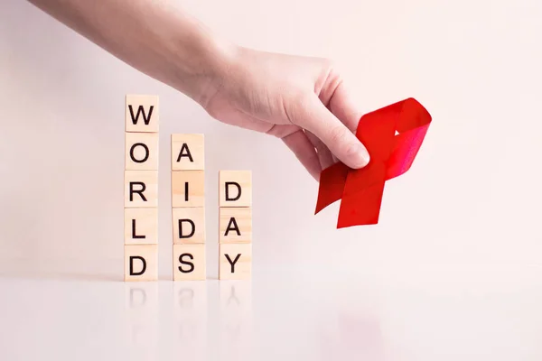 1 dicembre giornata mondiale aiuti fatta di lettere di legno e mano tenuta bymbol nastro rosso. AIDS, sensibilizzazione sull'HIV, diffusione dell'infezione, giornata della memoria, solidarietà con le persone affette da HIV. Giornata mondiale della salute — Foto Stock