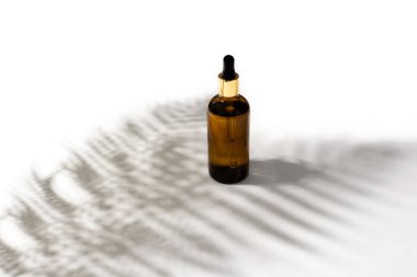 Serum, oil, acid, lotion in brown dropper glass bottle on white background with tropical leaves shadows, copy space. Spa product. Organic, natural cosmetic. Beauty, skincare concept.