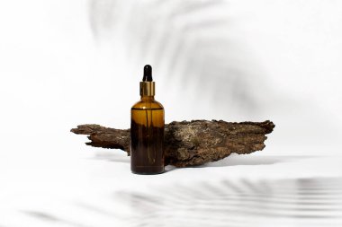 Serum, oil, acid, lotion in brown dropper glass and tree bark in front of white background with tropical leaves shadows, copy space. Spa product. Organic, natural cosmetic. Beauty, skincare concept.