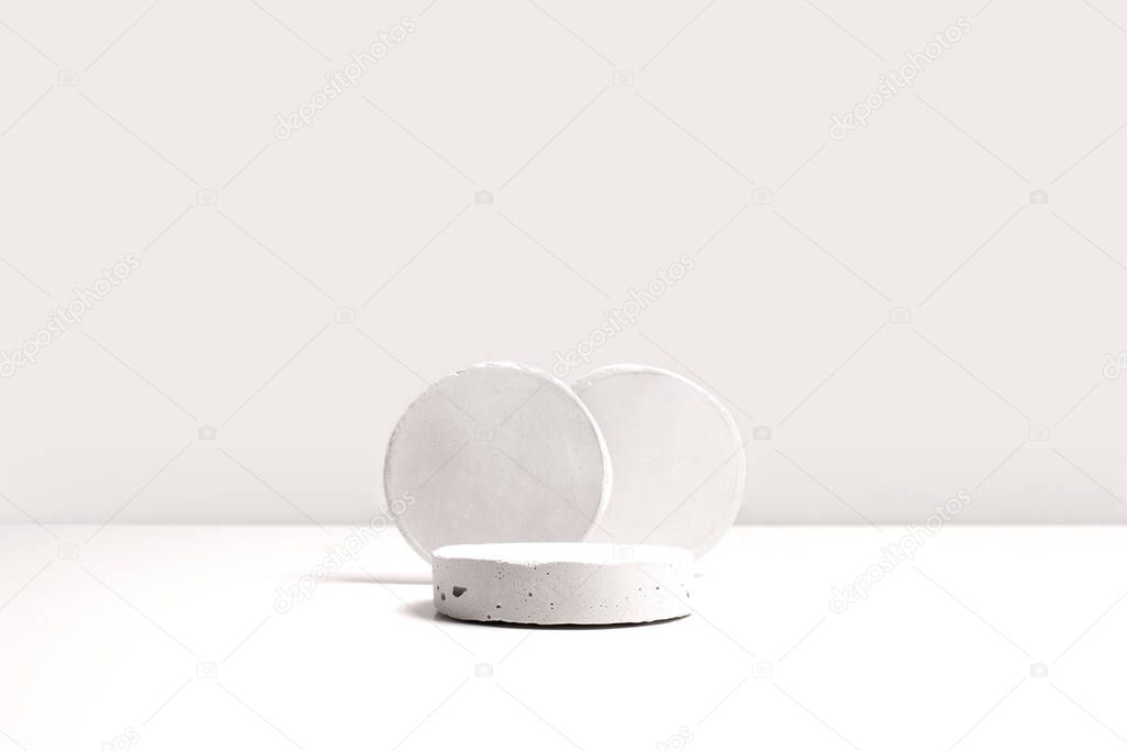 Gray cocncrete circle shaped pedestals on white table with copy space, side view. Podium mockup background for products. Advertising template. Stone platform. Abstract geometric pedestal.