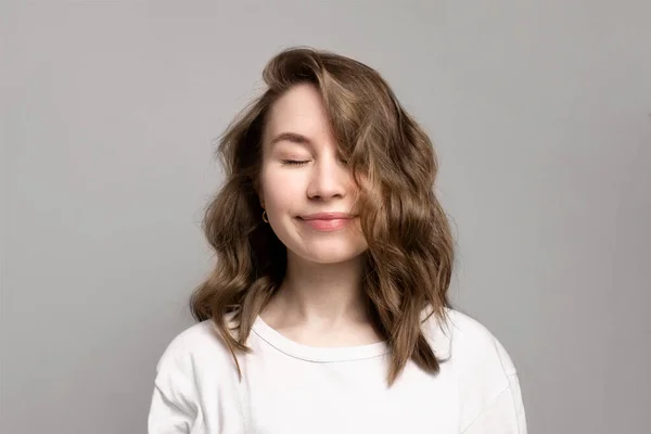 Portrait of happy smiling young woman with closed eyes, gray background, copy space. Beautiful caucasian girl with brown curly hairstyle. Cheerful, satisfied, dreamy expression face. Calmness, relax — Stock Photo, Image