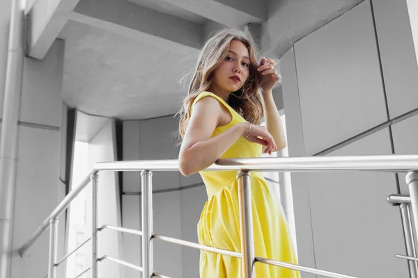 Young woman in illuminating yellow dress standing in front of gray wall, leaning on iron railings and looking at camera. 2021 Color Trends. Girl having fun. Urban style and fashion. Casual outfit — Stock Photo, Image