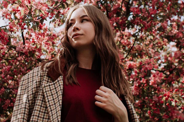 Smilende Ung Kvinde Jakke Stående Alene Blandt Lyserøde Blomster Blomstrende - Stock-foto