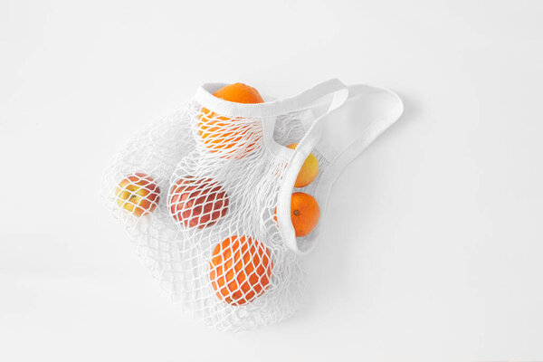 White mesh bag with fruits flat lay on white background top view. Eco friendly, reusable shopping bag. Oranges, apples, garnet in cotton knitted bag.