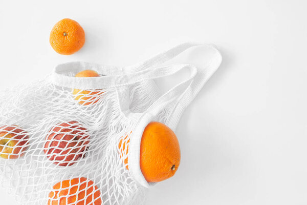White mesh bag with fruits flat lay on white background top view. Eco friendly, reusable shopping bag. Oranges, apples, garnet in cotton knitted bag.